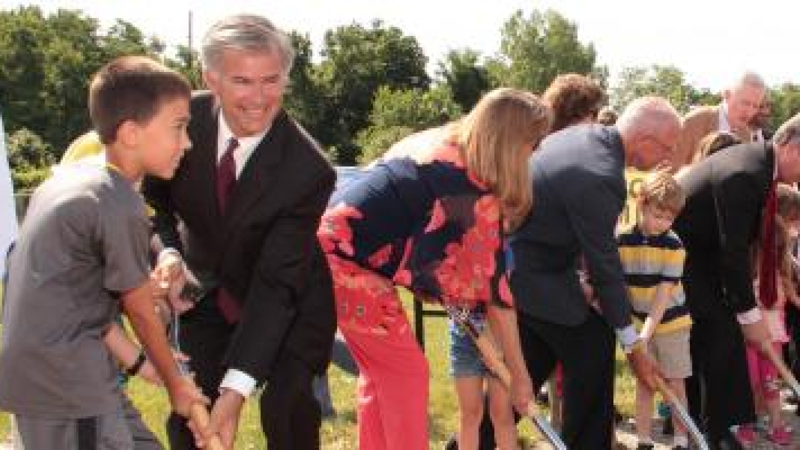 Community groundbreaking ceremony with a row of people with shovels in dirt