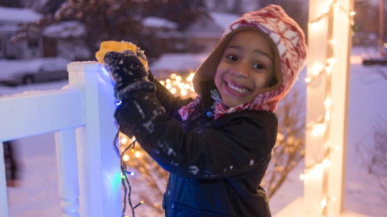 girl hanging holiday lights on a deck railing