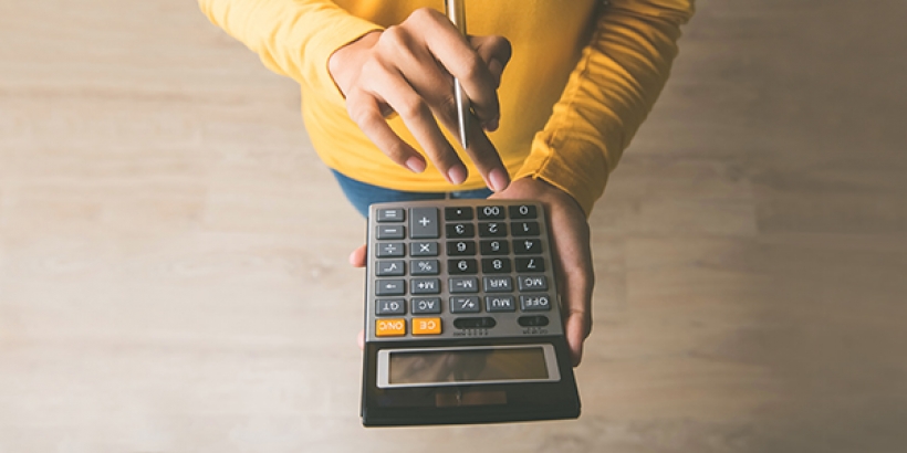 person with yellow shirt, pen in hand using calculator