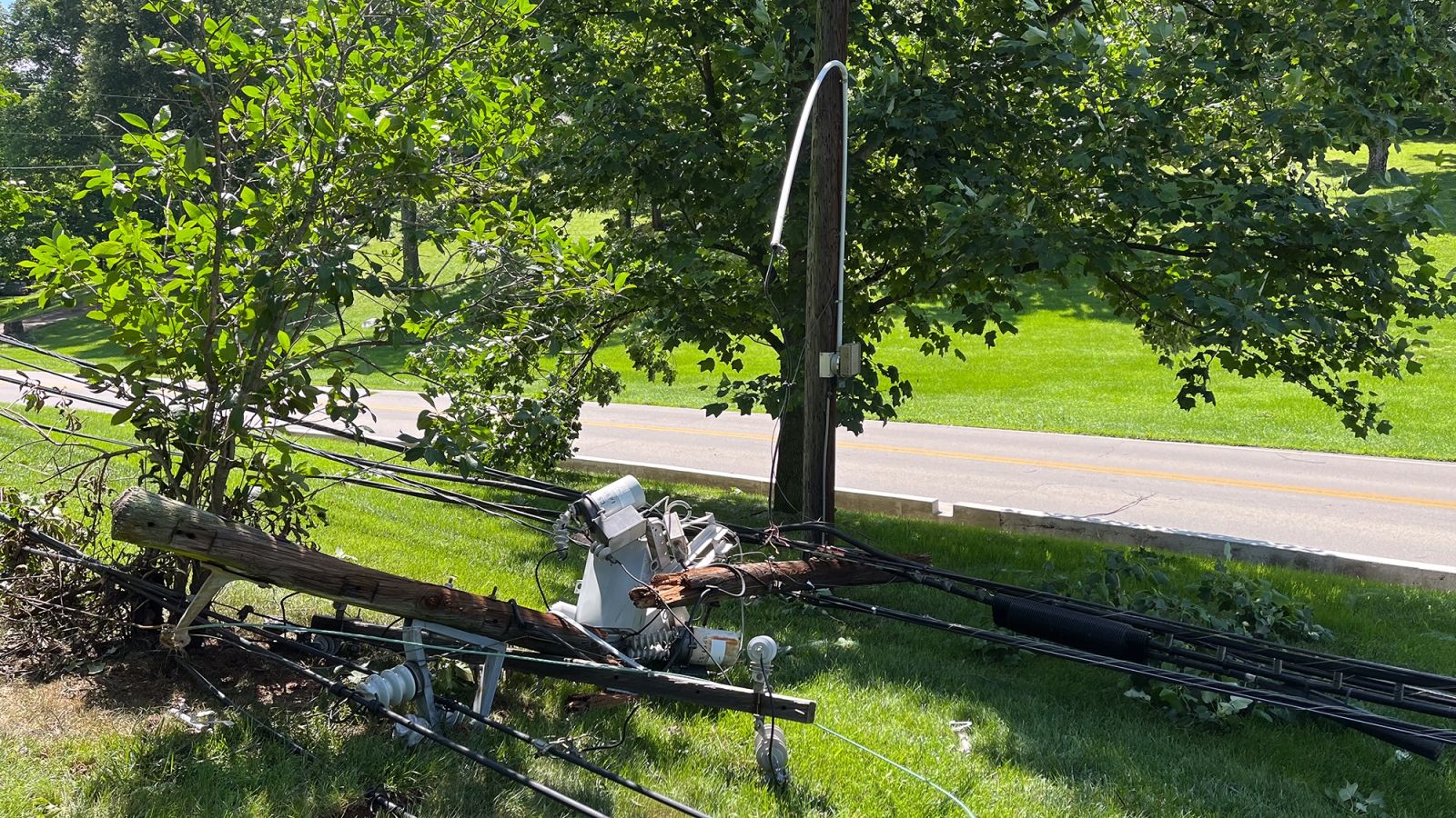 a broken pole with lines and transformer on the ground