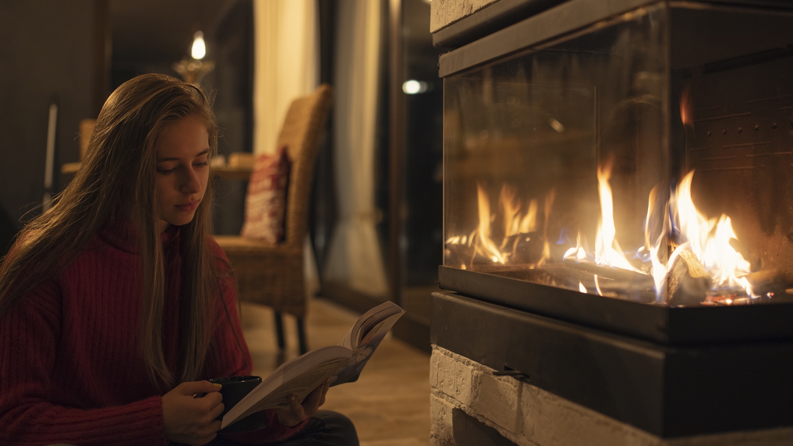 person sitting on floor reading a book in front of a fireplace