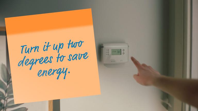 finger at thermostat with post-it note reading "Turn it up two degrees to save energy"