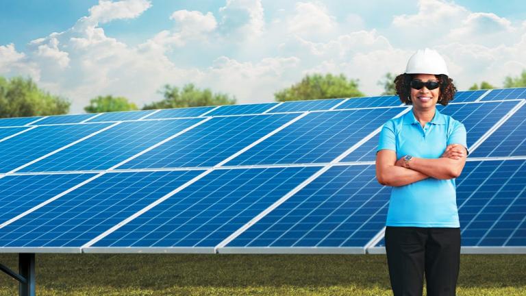 female employee with hard hat standing in front of solar panels
