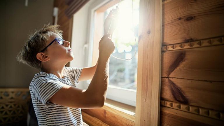 a boy wearing glasses lowering a window blind
