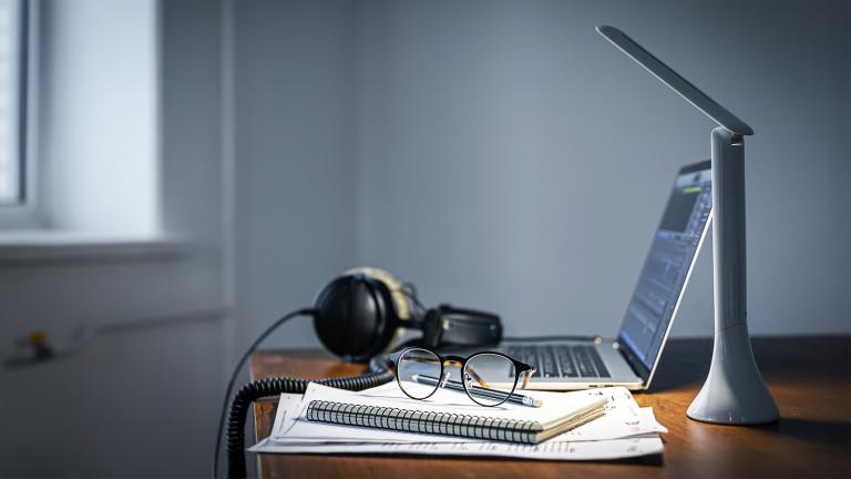 desk with a laptop, headset, notebook and desk lamp
