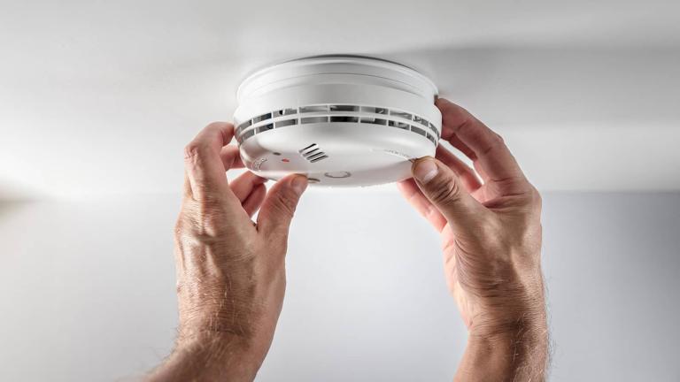 two hands replacing batteries on a smoke detector on a ceiling