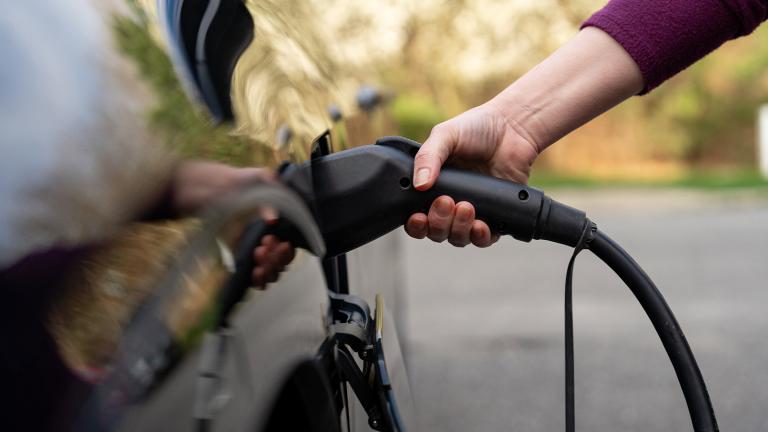 a hand holding an electric vehicle charger in a port on the side of a black car