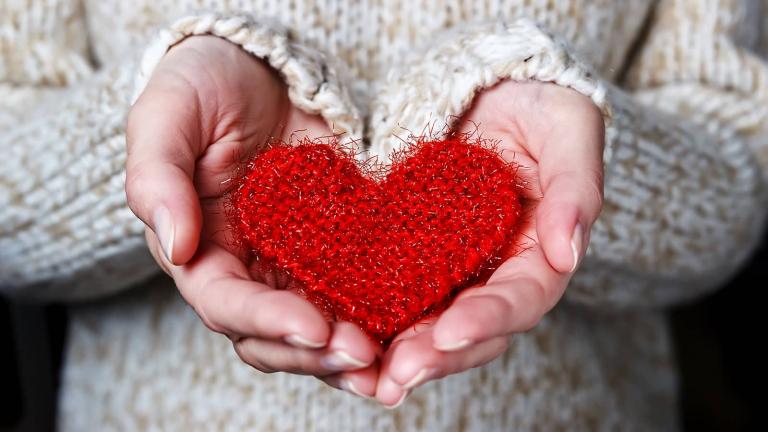person in a sweater holding a knitted heart in hands