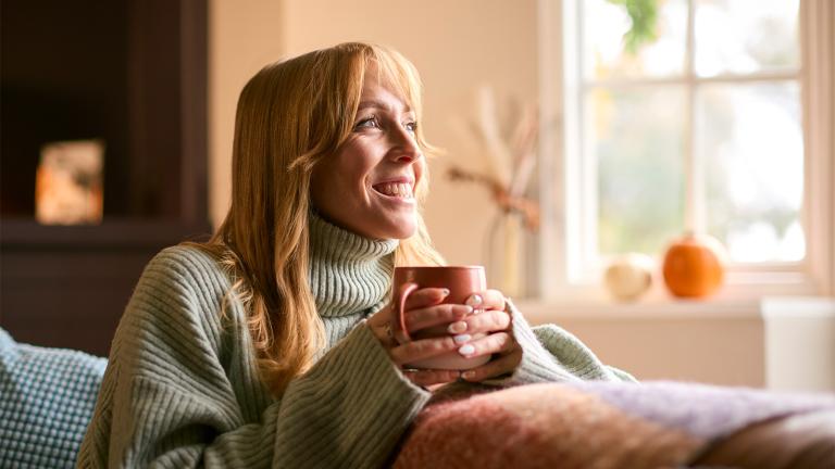 person sitting on a couch holding a warm mug looking out the window