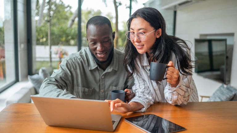 a couple holding mugs looking at a laptop