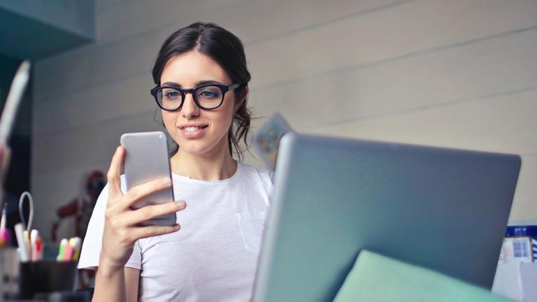 Customer looking at her phone sitting in front of laptop