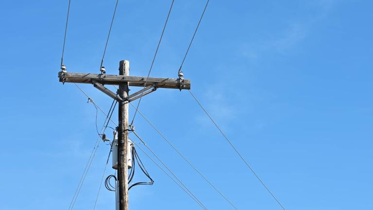a wooden pole with electric power lines and a transformer attached, with a blue sky in the background