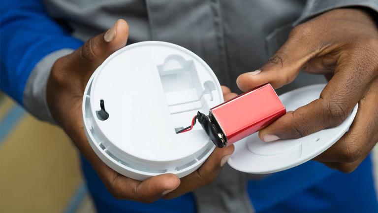 hands checking battery on smoke detector