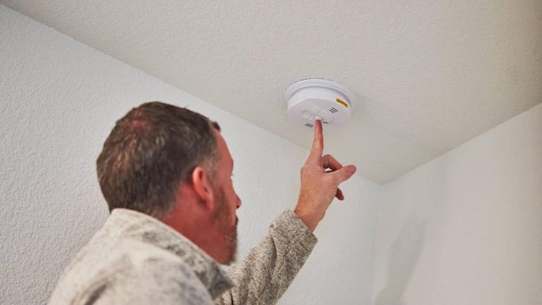 person testing smoke detector on a ceiling
