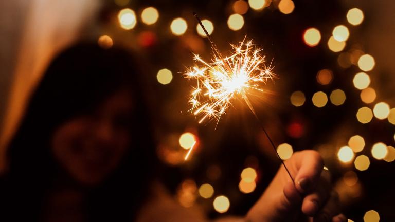 person holding a sparkler with a lighted tree in the background