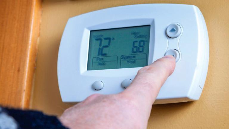 person turning down temperature on a digital thermostat