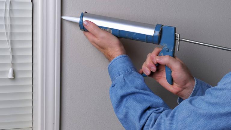 hands with a caulk gun sealing a window