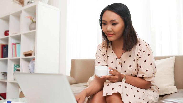 person sitting on couch with cup using a laptop