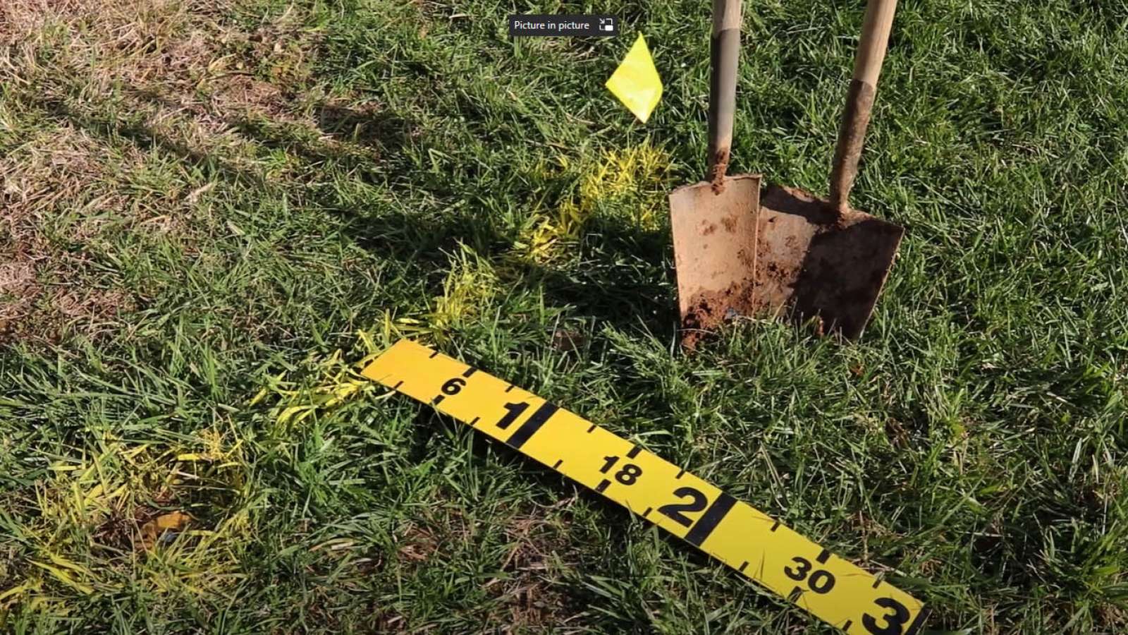 two shovels in grass yard with yellow flag and paint marker