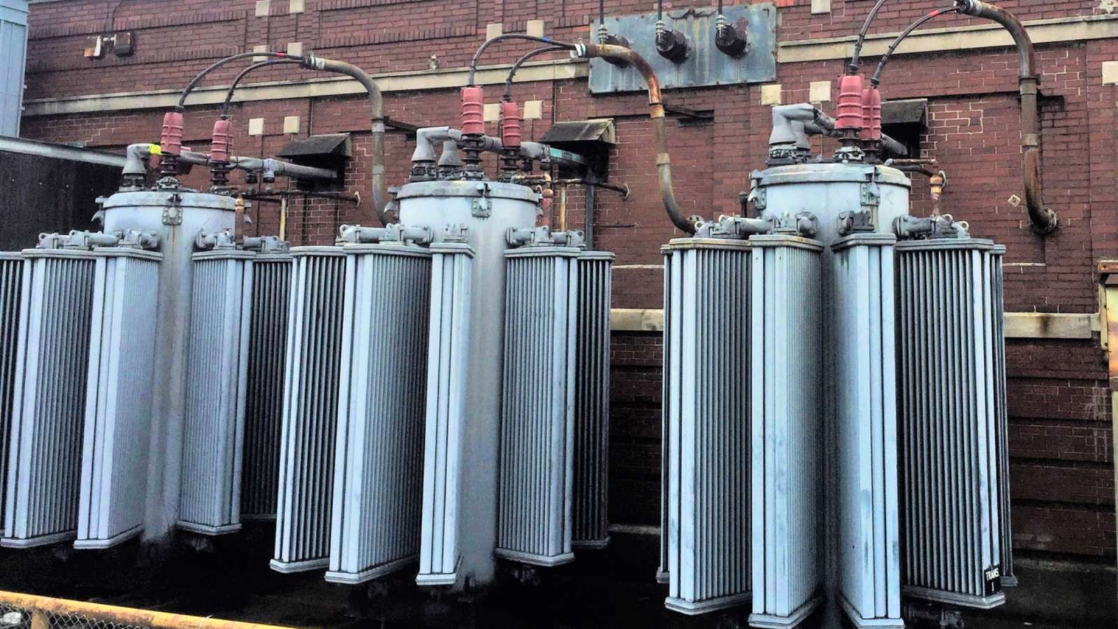 three 100-year-old transformer at a substation with a brick wall in the background