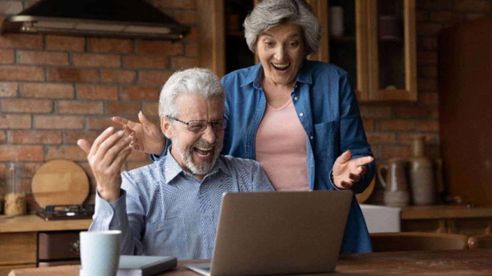 couple in kitchen smiling at laptop on table