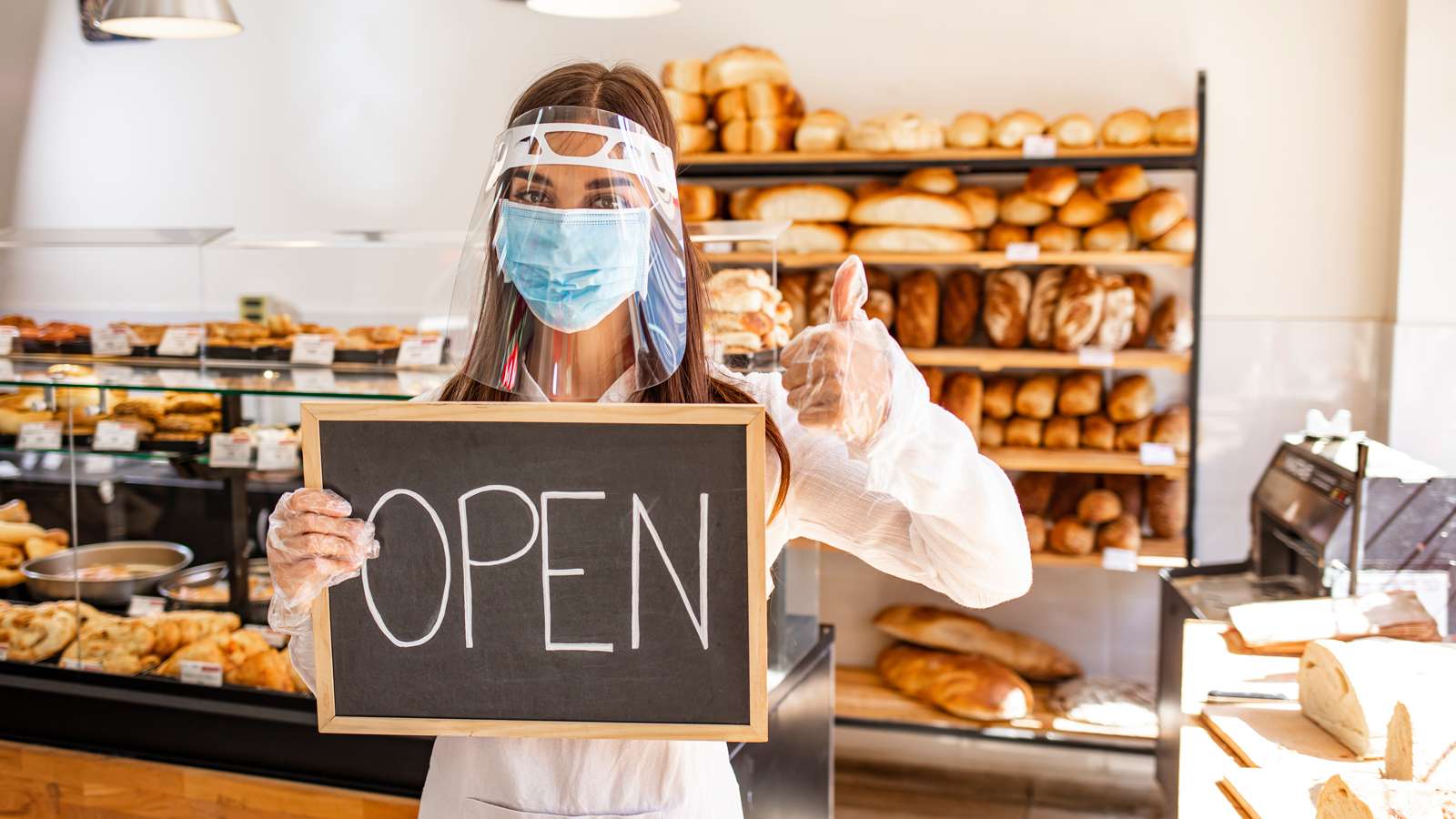 Business owner with face mask holding open sign
