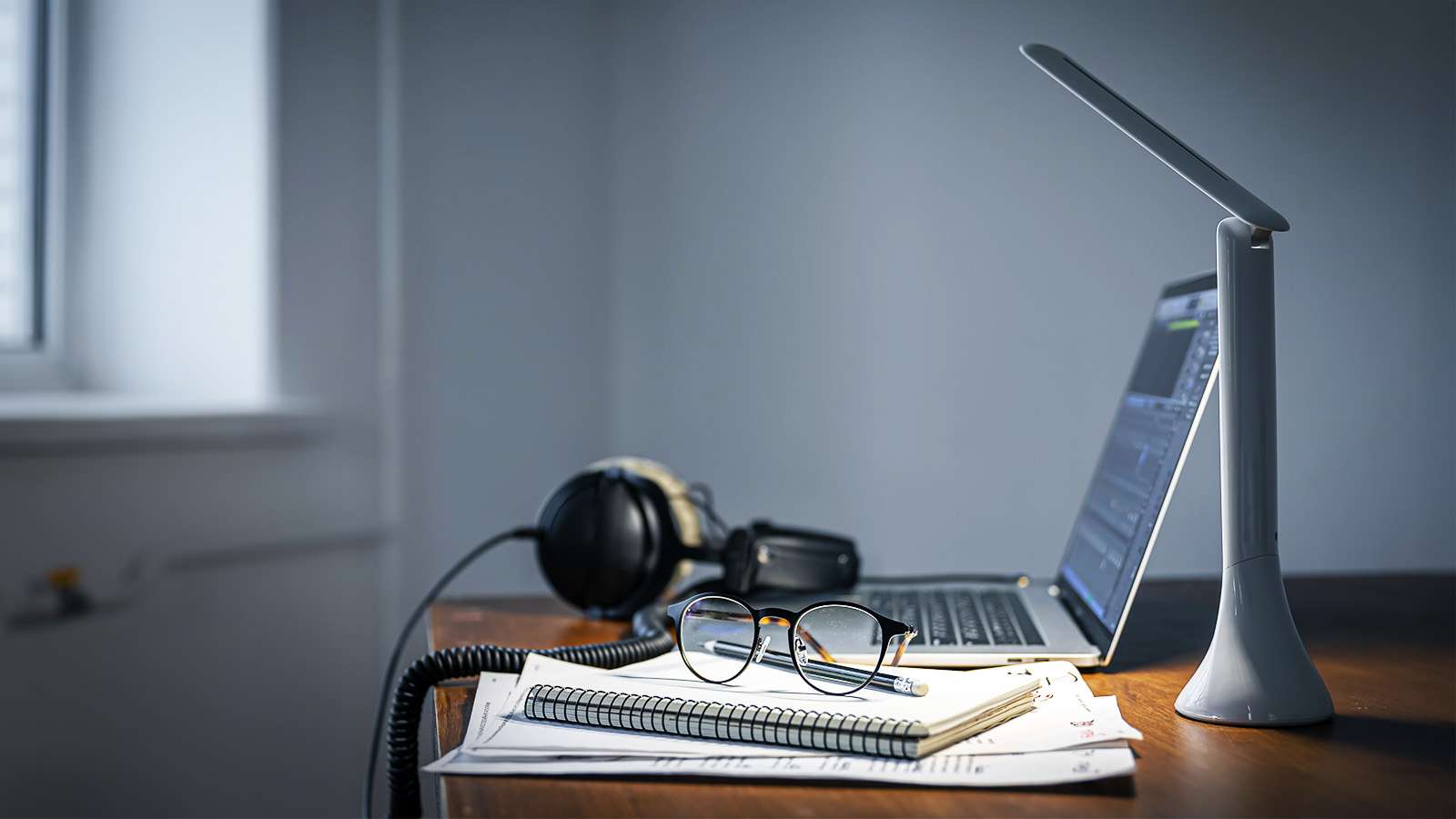 desk with a laptop, headset, notebook and desk lamp