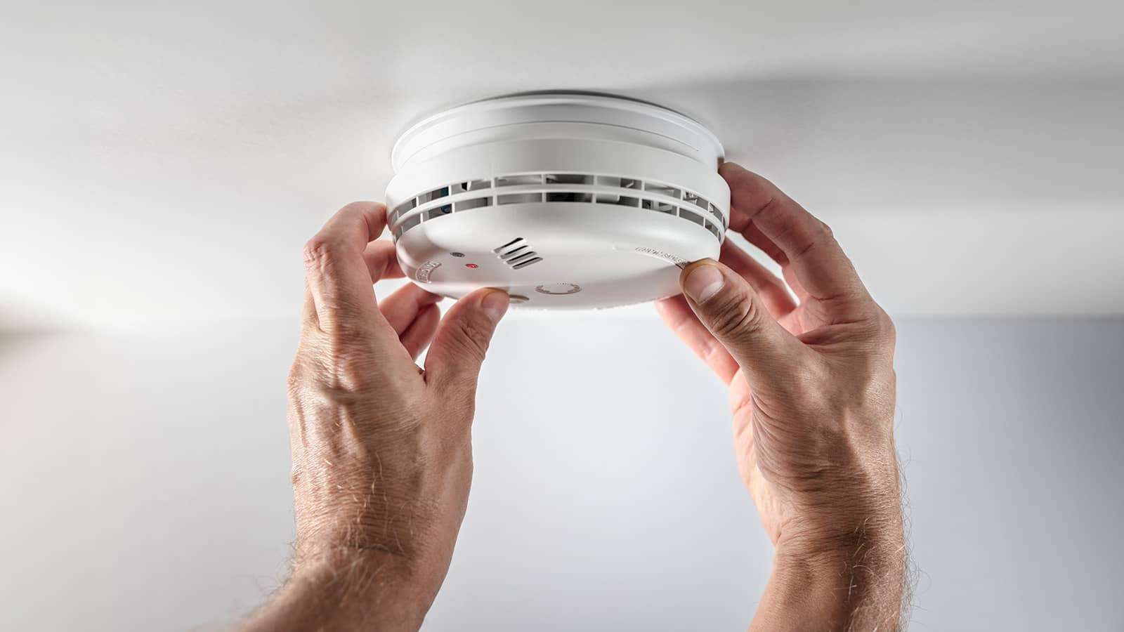 two hands replacing batteries on a smoke detector on a ceiling