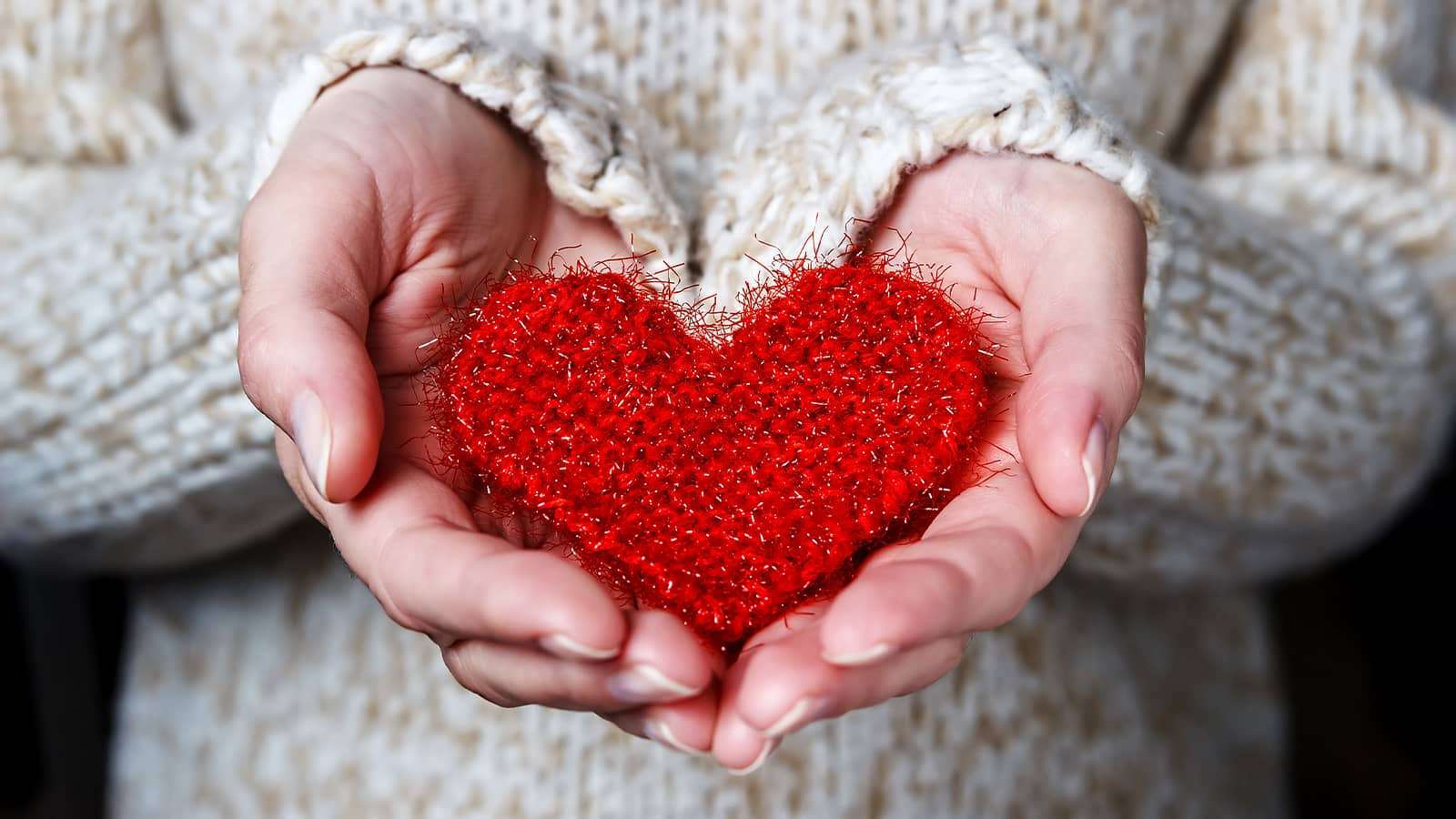 person in a sweater holding a knitted heart in hands