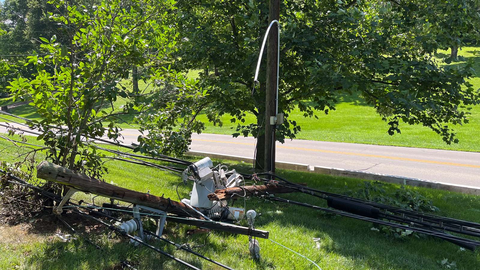 a broken pole with lines and transformer on the ground