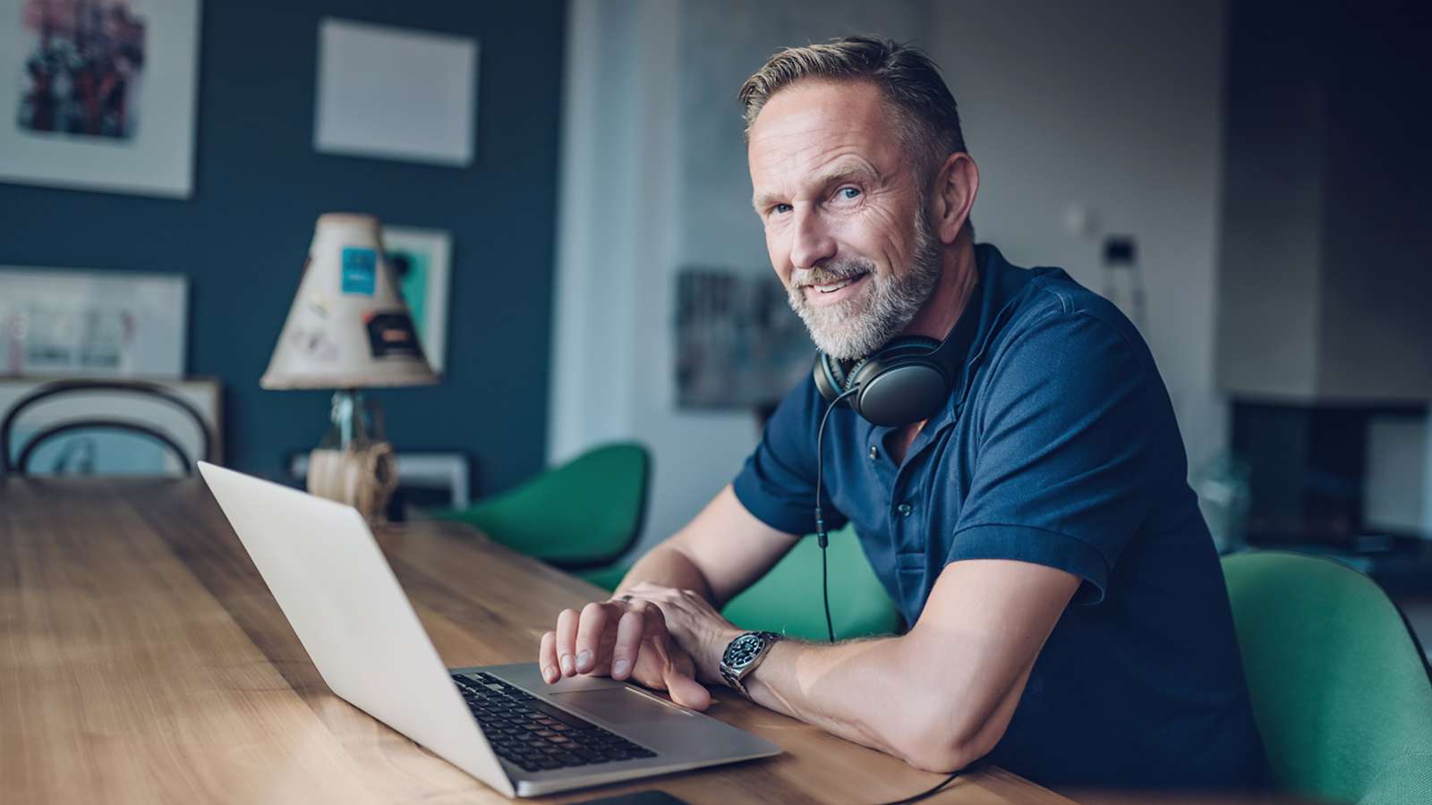 person at a desk on a laptop with headphones around neck