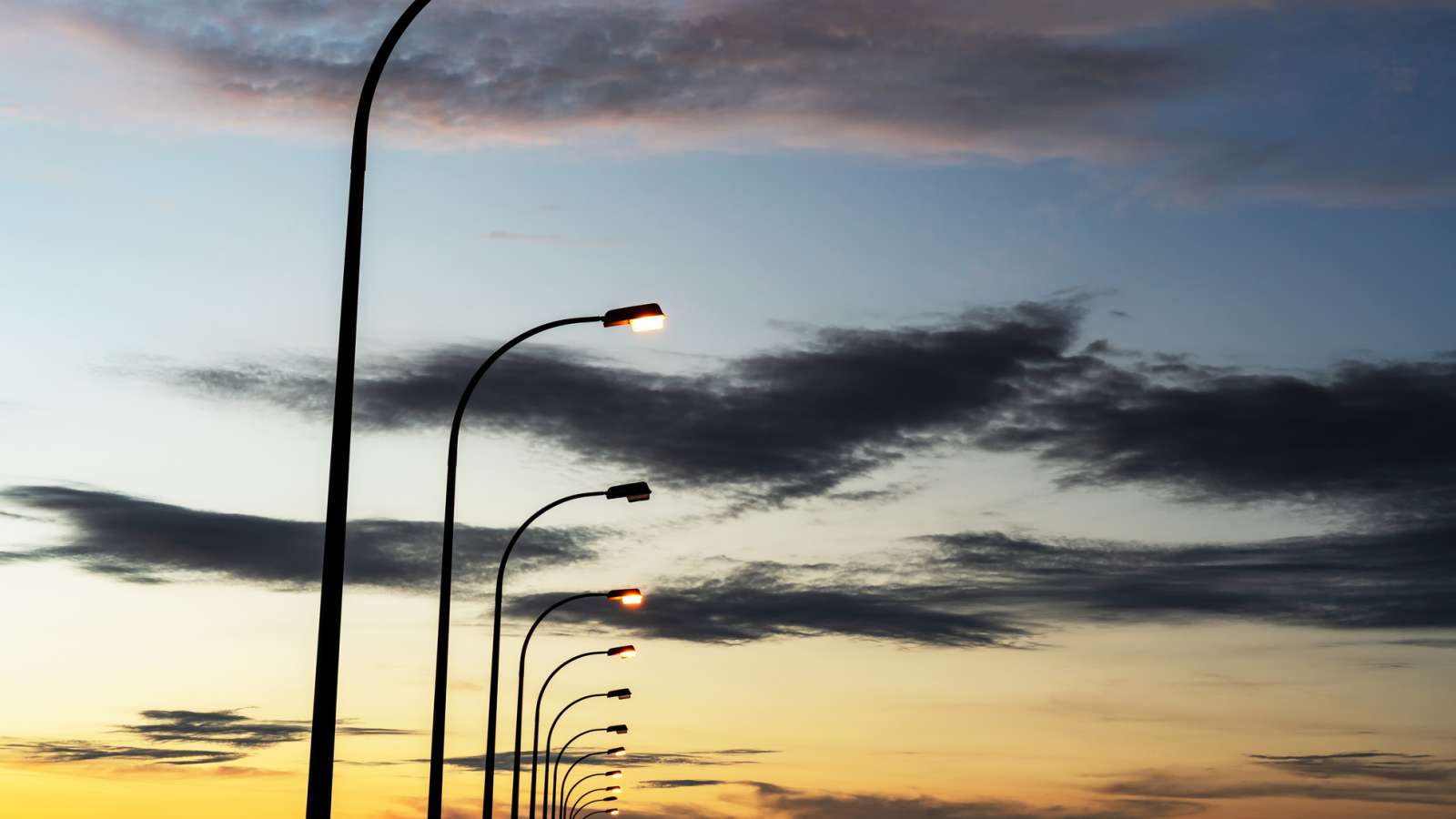 A row of streetlights against a background of a twilight sky with wispy clouds.
