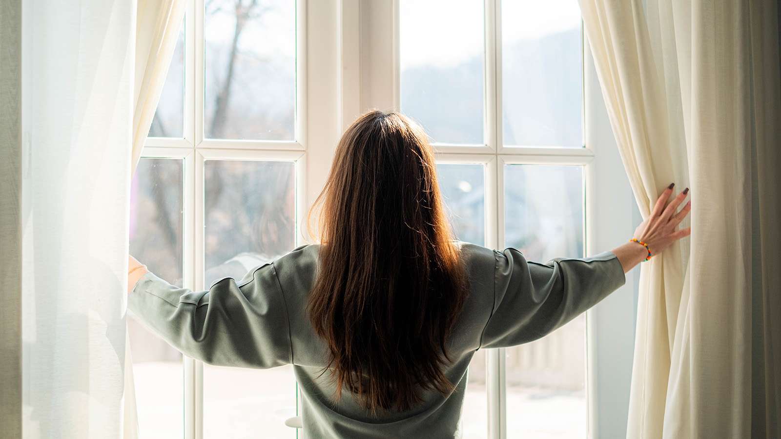 person standing at window holding curtains open