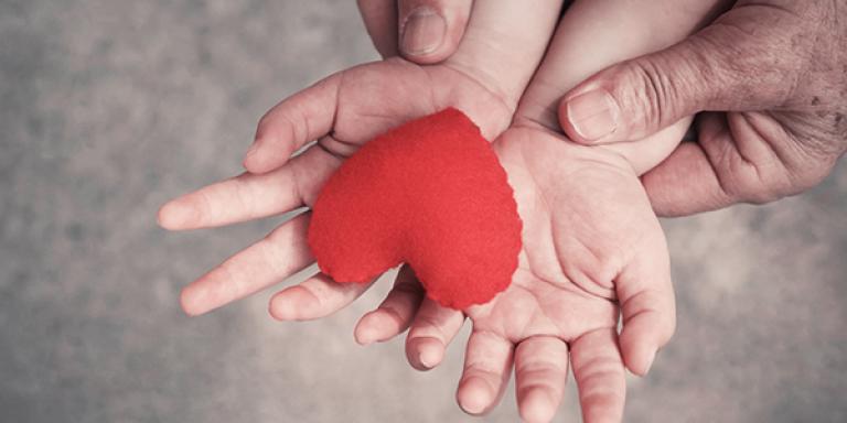 Child hands holding plush heart with adult hands holding the childs