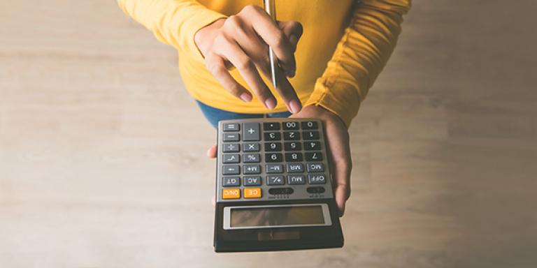 person with yellow shirt, pen in hand using calculator